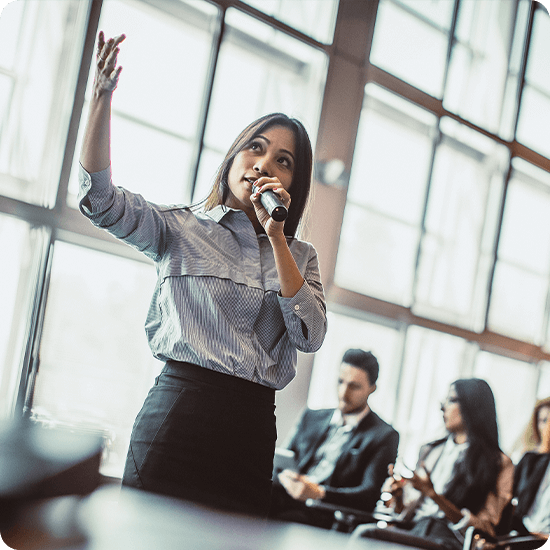 A woman with a microphone speaking to guests in an office